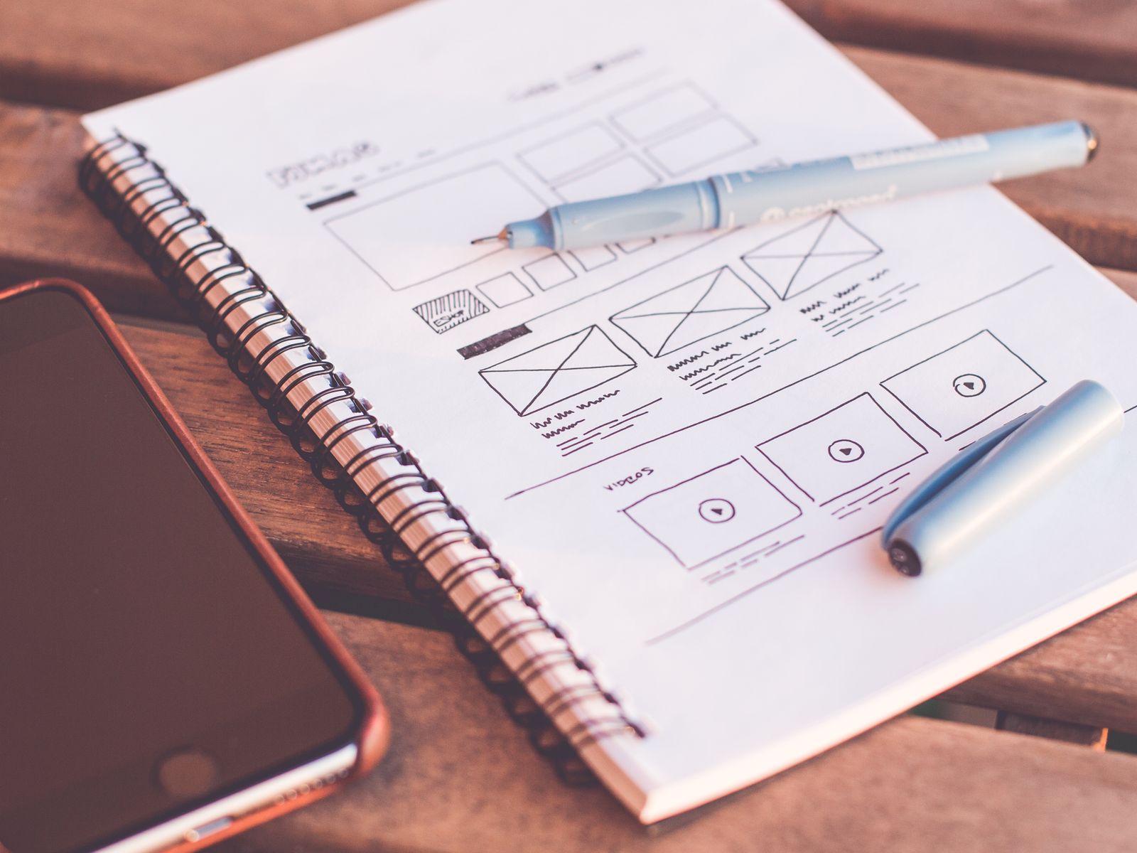 Boceto a mano de la estructura de una página web en una libreta junto a un teléfono